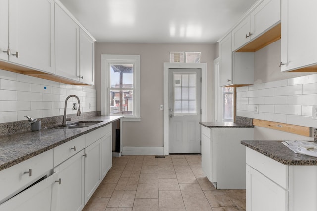 kitchen featuring baseboards, decorative backsplash, dark stone countertops, a sink, and light tile patterned flooring