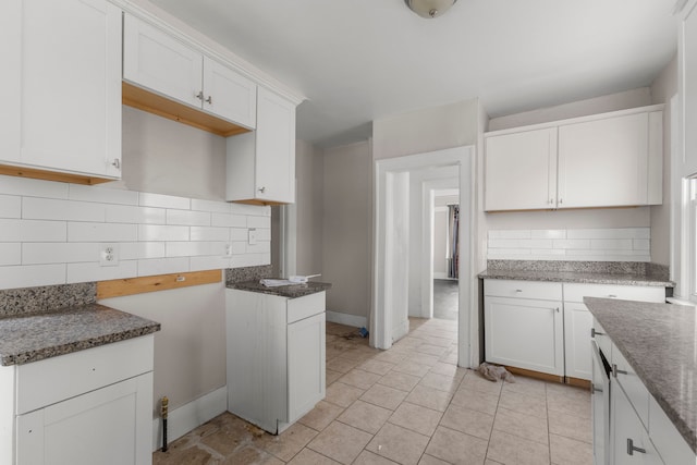 kitchen featuring stone counters, light tile patterned floors, backsplash, white cabinets, and baseboards