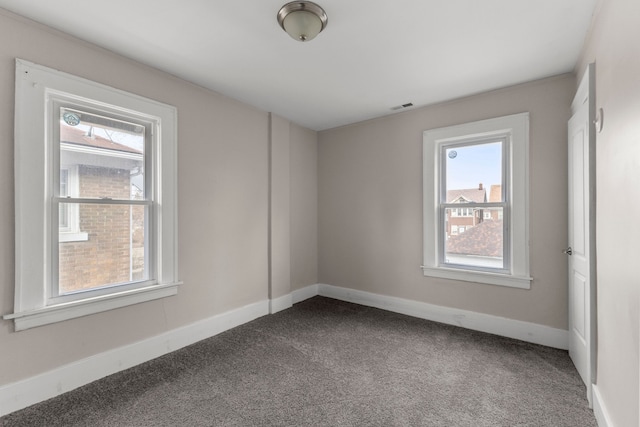 spare room with dark colored carpet, visible vents, and baseboards