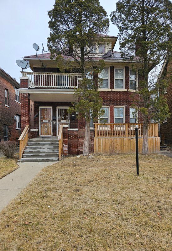 view of front of property with brick siding, a front yard, and a balcony