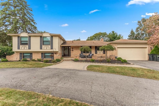 tri-level home featuring aphalt driveway, a garage, brick siding, a front lawn, and a chimney