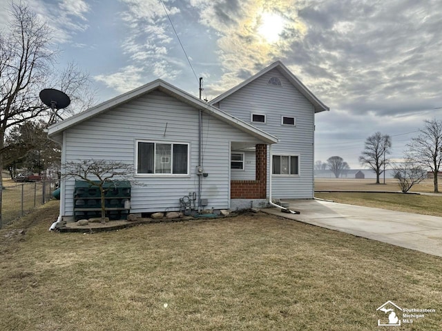 rear view of property with concrete driveway, a lawn, and fence