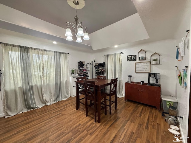 dining area featuring wood finished floors, a raised ceiling, and a notable chandelier