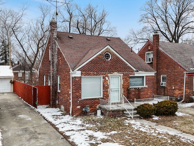 bungalow with roof with shingles, brick siding, a chimney, and an outdoor structure