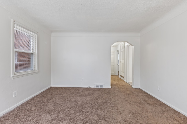 empty room featuring arched walkways, a textured ceiling, carpet, and visible vents