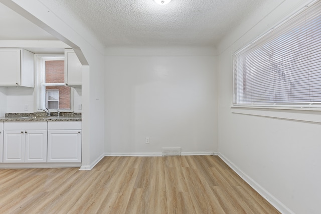 unfurnished dining area with light wood-type flooring, baseboards, visible vents, and a textured ceiling