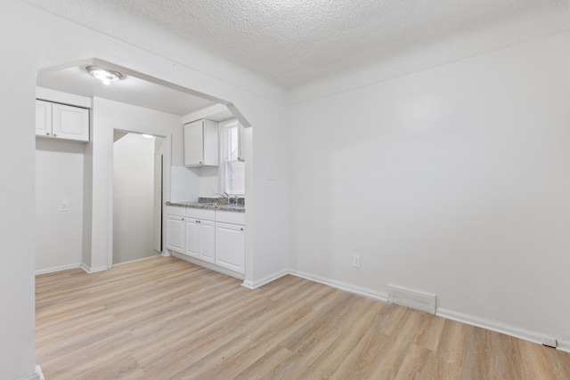 kitchen featuring arched walkways, a textured ceiling, visible vents, white cabinets, and light wood finished floors