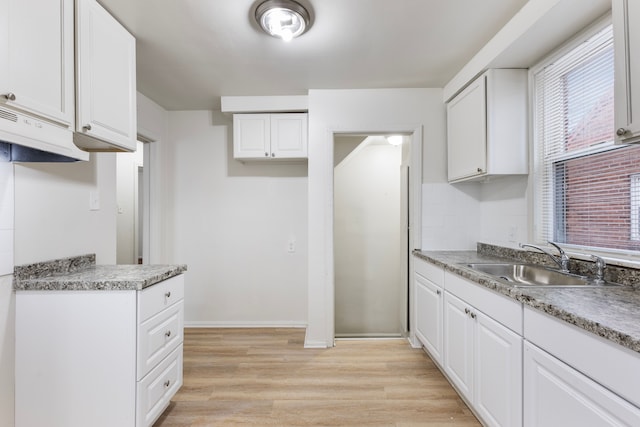 kitchen with tasteful backsplash, white cabinets, a sink, and light wood finished floors