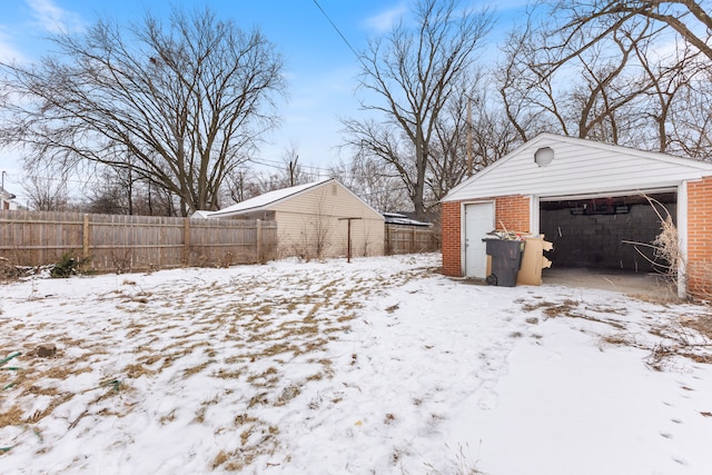 yard covered in snow with fence, a detached garage, and an outdoor structure