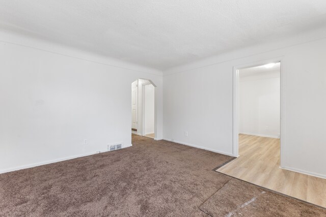 spare room with arched walkways, visible vents, carpet flooring, a textured ceiling, and baseboards