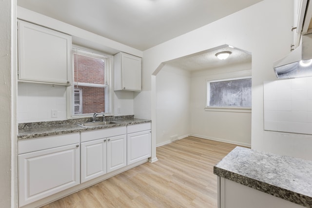 kitchen featuring a sink, baseboards, white cabinets, decorative backsplash, and light wood finished floors