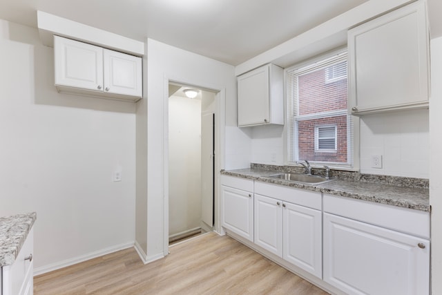 kitchen with a sink, white cabinetry, baseboards, backsplash, and light wood finished floors