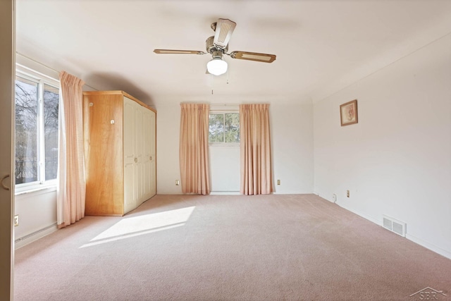 unfurnished bedroom featuring visible vents, baseboard heating, a ceiling fan, and light colored carpet