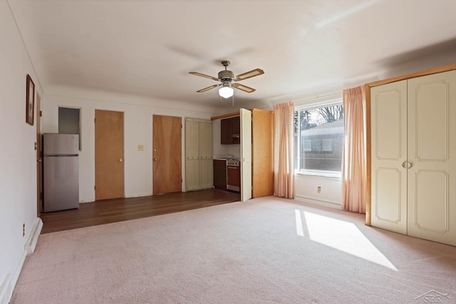 unfurnished bedroom featuring light carpet, a ceiling fan, multiple closets, and freestanding refrigerator