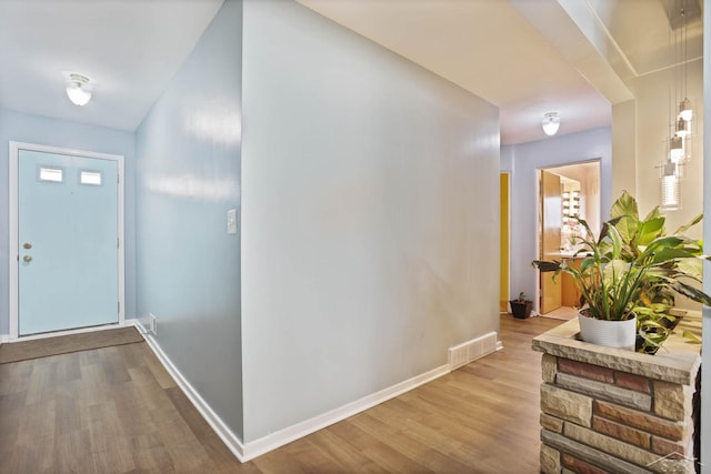 corridor featuring visible vents, baseboards, and wood finished floors