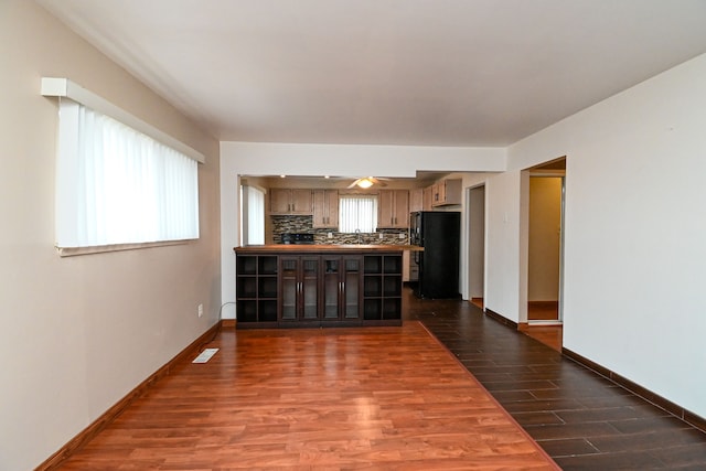 interior space with baseboards, a peninsula, dark wood-style flooring, freestanding refrigerator, and tasteful backsplash