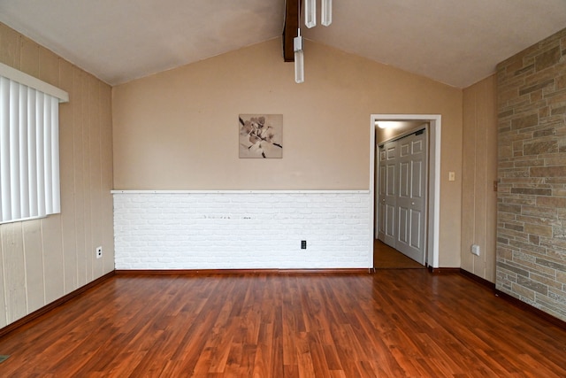 unfurnished room featuring lofted ceiling with beams, wood finished floors, a wainscoted wall, and brick wall