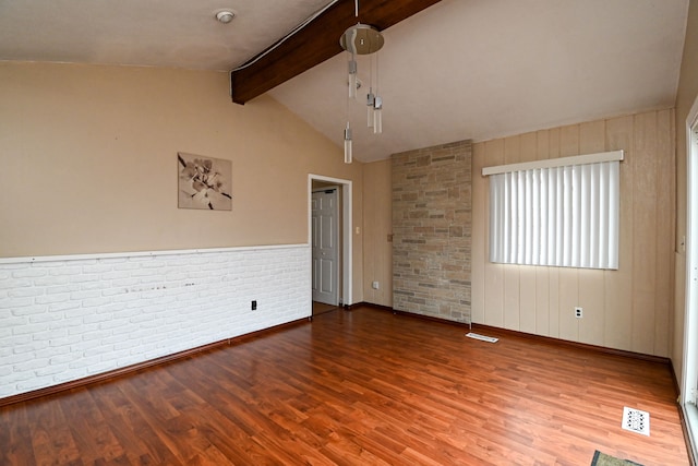 unfurnished room with visible vents, brick wall, vaulted ceiling with beams, and wood finished floors