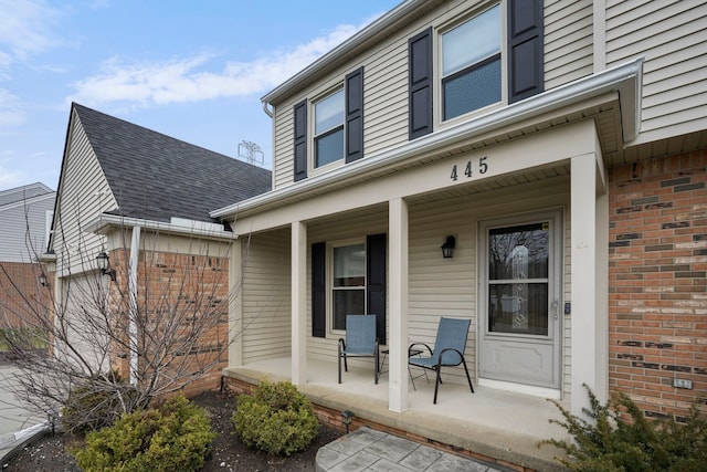 view of exterior entry featuring a porch, brick siding, and a shingled roof