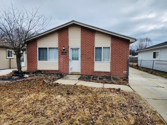 view of front of property featuring brick siding, concrete driveway, and fence