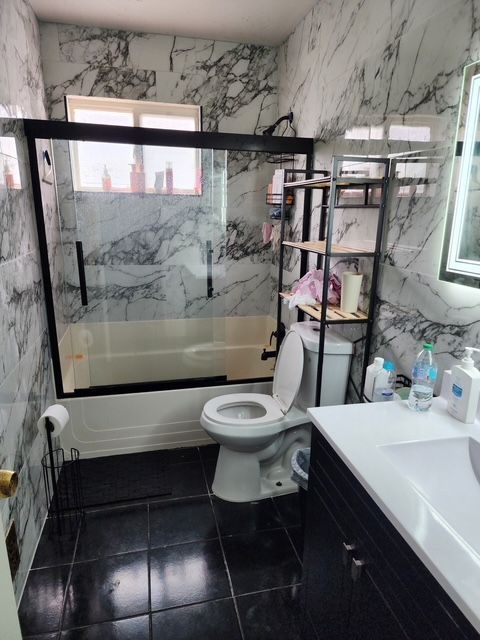 bathroom with toilet, enclosed tub / shower combo, tile patterned flooring, vanity, and tile walls