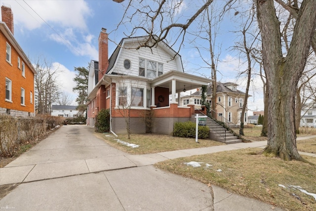 view of front facade with brick siding, a chimney, and a gambrel roof