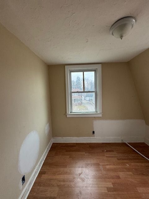 additional living space with a textured ceiling, wood finished floors, and baseboards