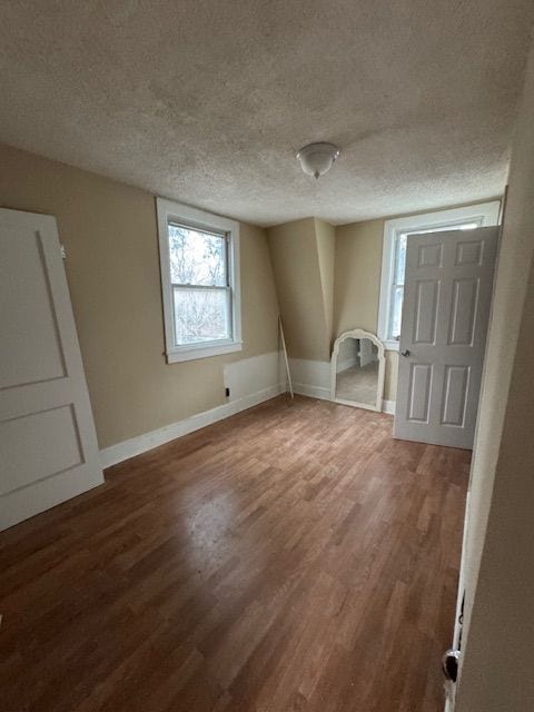 unfurnished bedroom featuring a textured ceiling, baseboards, and wood finished floors