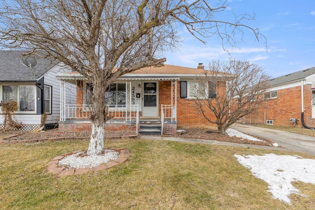 bungalow featuring driveway, brick siding, a chimney, a porch, and a front yard