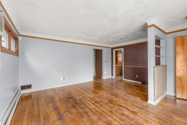 empty room with visible vents, crown molding, baseboard heating, and wood finished floors