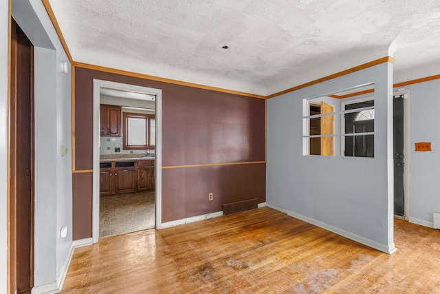 unfurnished room featuring light wood finished floors, baseboards, visible vents, ornamental molding, and a textured ceiling