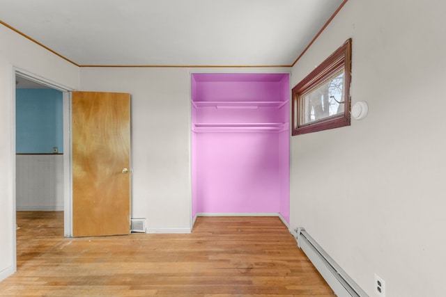 empty room with a baseboard heating unit, wood finished floors, visible vents, and crown molding