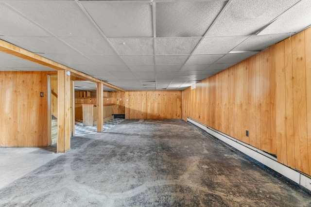 finished basement with a baseboard heating unit, a drop ceiling, and wooden walls