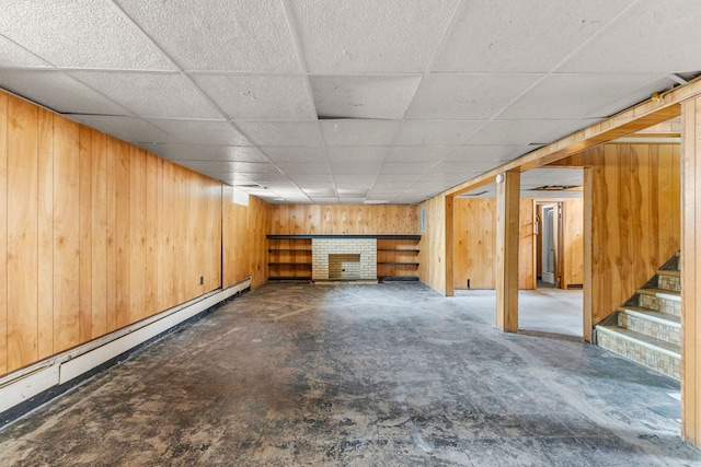 finished basement with a paneled ceiling, wood walls, a fireplace, baseboard heating, and stairway