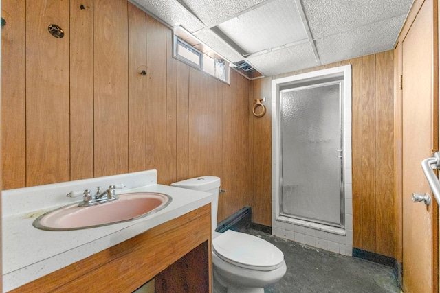 full bathroom with a drop ceiling, toilet, wood walls, vanity, and a stall shower