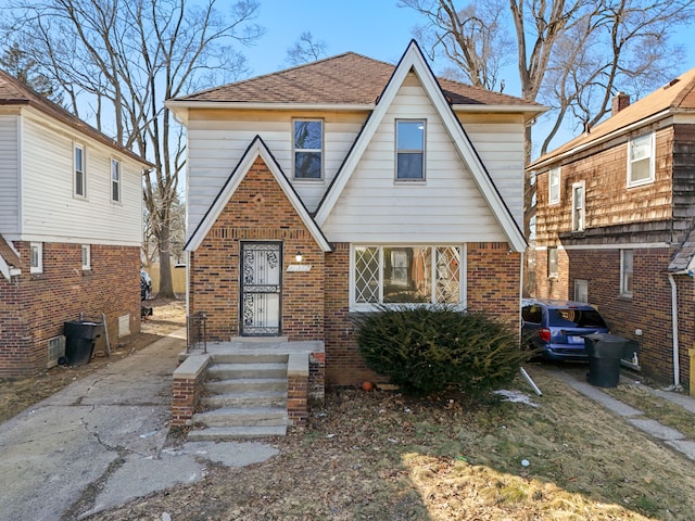 tudor-style house with roof with shingles and brick siding