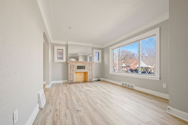 unfurnished living room featuring arched walkways, a fireplace, wood finished floors, visible vents, and baseboards