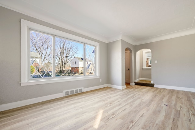 empty room with arched walkways, visible vents, baseboards, light wood-type flooring, and crown molding