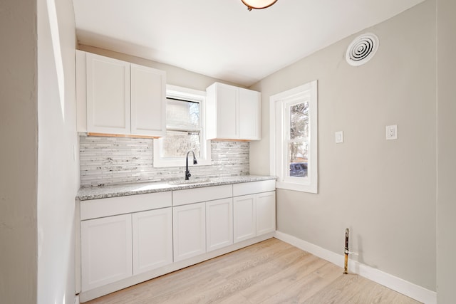 kitchen with visible vents, backsplash, white cabinets, a sink, and baseboards