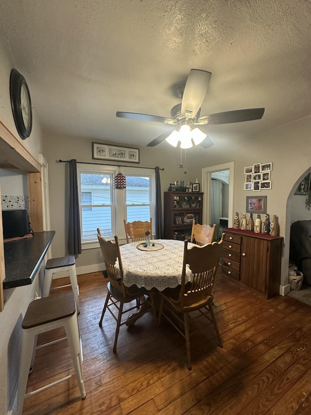 dining room featuring a textured ceiling, dark wood finished floors, and a ceiling fan