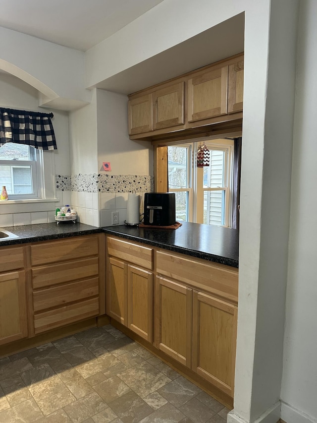 kitchen featuring stone finish flooring, dark countertops, and backsplash