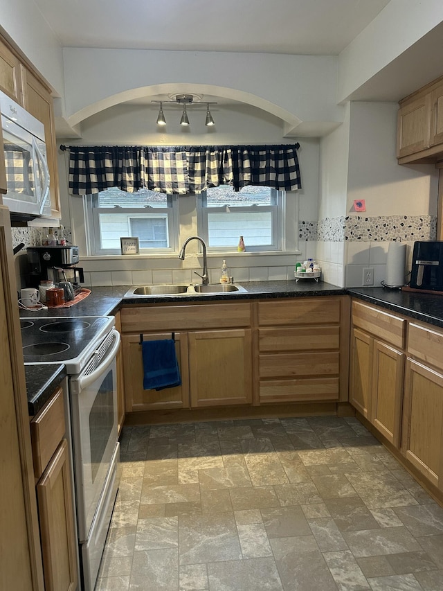 kitchen with dark countertops, electric range oven, white microwave, stone finish floor, and a sink