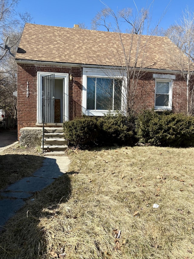 view of front of property with a shingled roof and brick siding