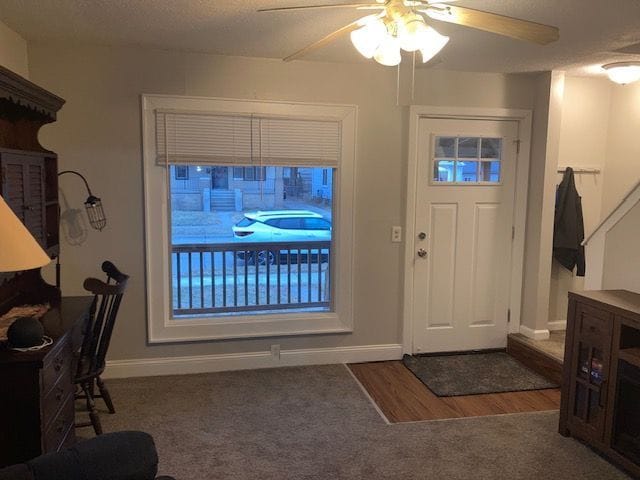 foyer entrance with carpet flooring, ceiling fan, baseboards, and wood finished floors