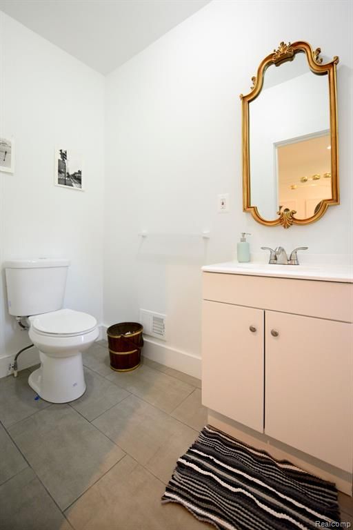 half bathroom featuring visible vents, toilet, vanity, tile patterned flooring, and baseboards