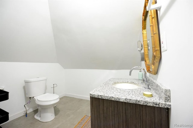 bathroom with toilet, lofted ceiling, baseboards, and vanity