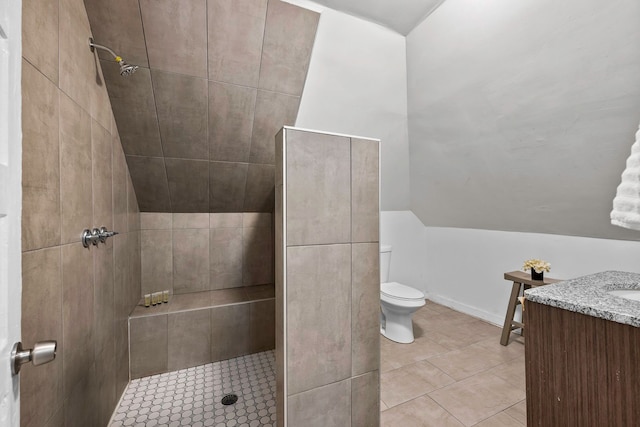 bathroom featuring lofted ceiling, tiled shower, vanity, and toilet