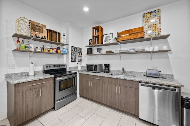 kitchen with stainless steel appliances, light stone countertops, a sink, and open shelves