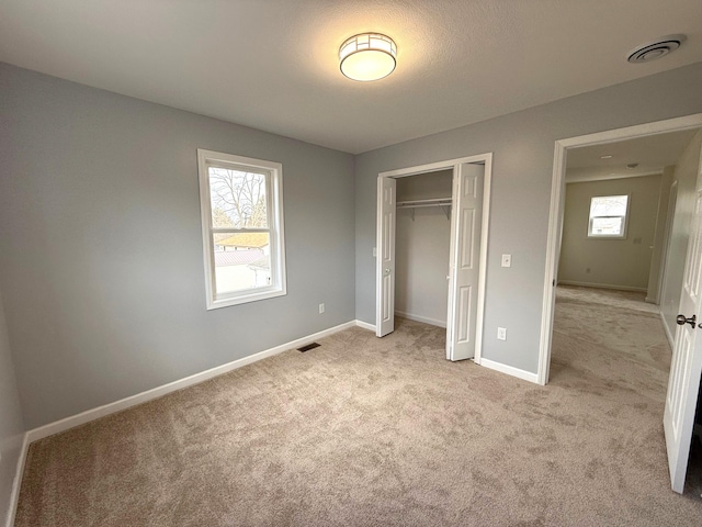 unfurnished bedroom with light carpet, baseboards, visible vents, and a closet