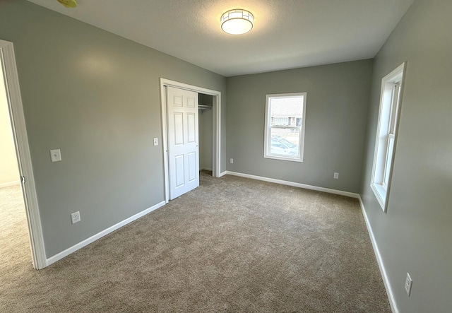 unfurnished bedroom featuring carpet, a closet, a textured ceiling, and baseboards